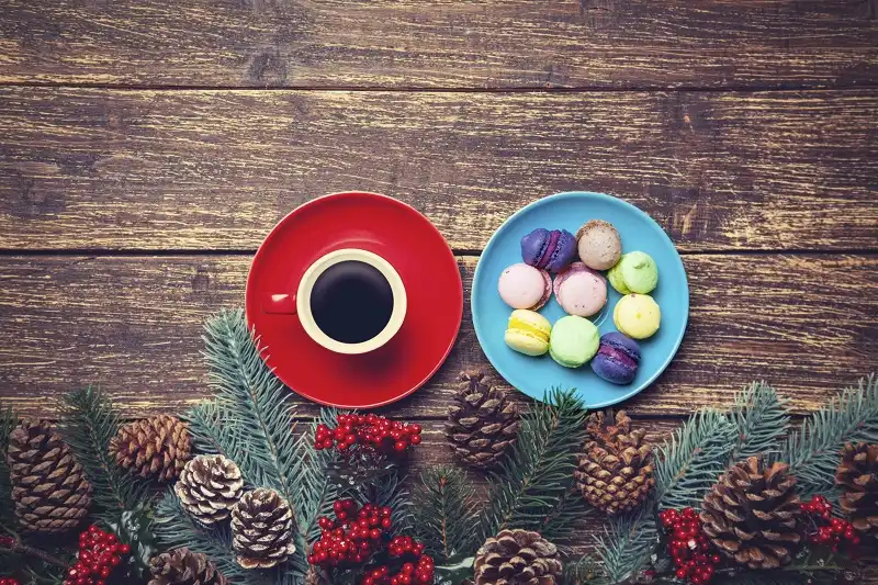 Cup of coffee and macaron near pine branches on a wooden table.