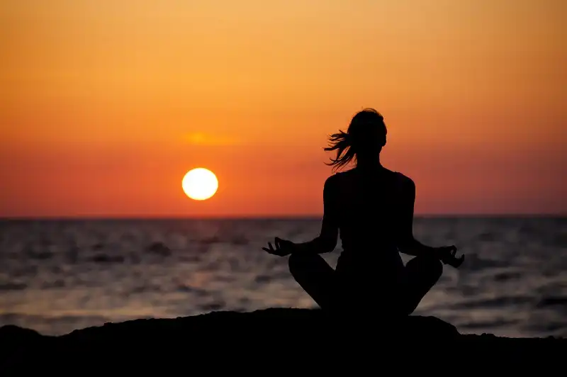 Silhouette of young woman in lotus position sitting on the beach and medditating