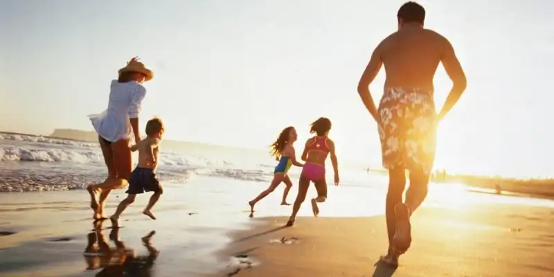 Family running on beach at sunset, rear view