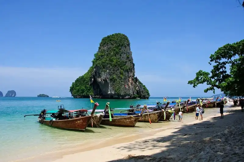 A groups of boats sit on the beach in front of one of the famous karsts (rock formations) at Phra Nang Beach in Krabi, Thailand.