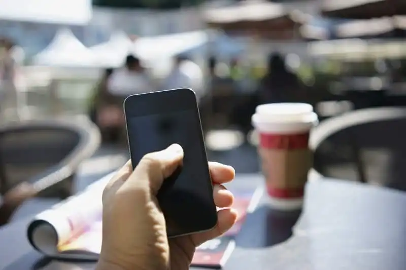 holding mobile phone with outdoor seats of a cafe as background
