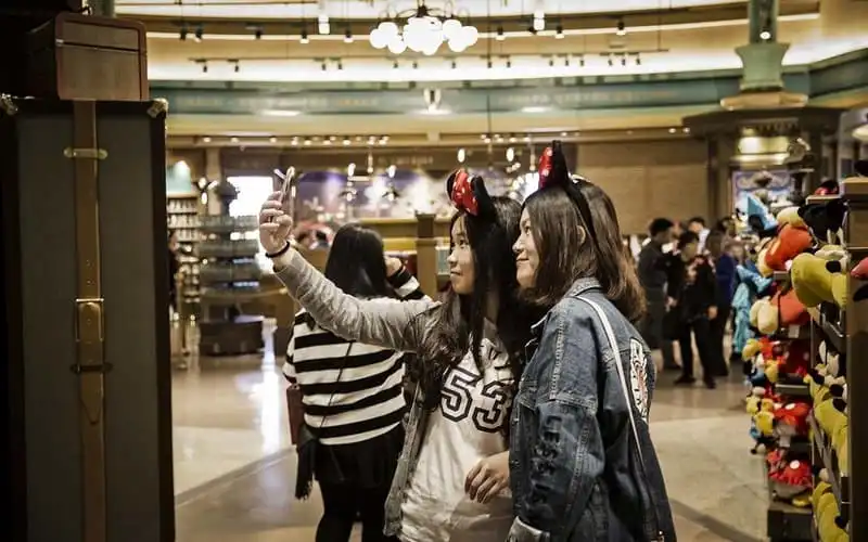 Visitors wearing Minnie Mouse ears pose for a selfie photograph inside a World of Disney store at the Disneytown retail area of Walt Disney Co.'s Disneyland Resort in Shanghai, China, on Saturday, May 7, 2016. Disney employees and partners will get a sneak peek of the $5.5 billion Shanghai Disneyland from this weekend, as the world's largest entertainment company gets set for next month's official opening of its first theme park in mainland China. Photographer: Qilai Shen/Bloomberg via Getty Images
