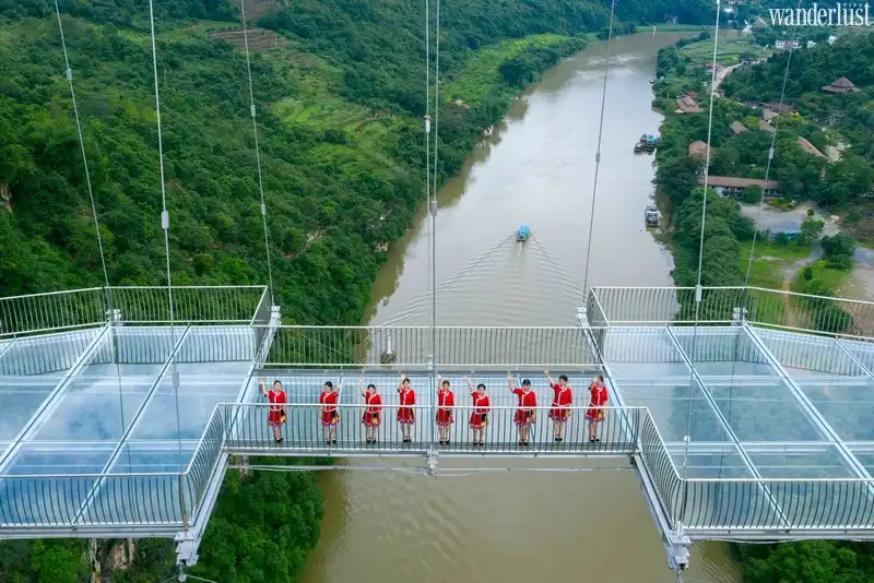 Phần đáy kính của cây cầu được cấu tạo từ 3 lớp kính cường lực, mỗi lớp dày khoảng 4.5cm. Với thiết kế kính hoàn toàn trong suốt có thể nhìn xuyên thấu, du khách có cơ hội trải nghiệm cảm giác như đang bay lơ lửng phía trên dòng sông chảy xiết. Từ trên cầu nhìn xuống, bạn thỉnh thoảng sẽ bắt gặp một vài chiếc thuyền chở khách thưởng ngoạn cảnh sắc tuyệt diệu của miền sông nước trù phú. Cây cầu kính kỷ lục có thể phục vụ tới 500 du khách cùng một lúc. Ngoài phần lan can được làm từ chất liệu thép không gỉ, cây cầu còn có các dây cáp chính màu đỏ bắt mắt, vô cùng nổi bật trên nền đồi núi xanh tươi. Quá trình xây dựng cầu kính hoàn tất vào đầu năm 2020. Sau đó, Tổ chức Kỷ lục Guinness Thế giới chính thức công nhận đây là cây cầu thủy tinh dài nhất thế giới vào mùa hè năm nay.